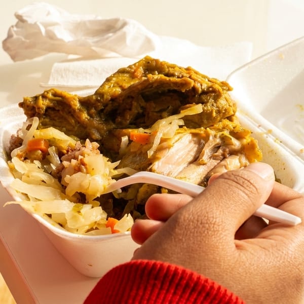 A person's hand holds a fork, eating curry chicken and rice from a white takeout container.
