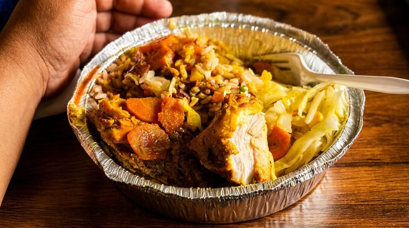 Curried chicken, rice, and cabbage in a foil takeout container with a white plastic fork.